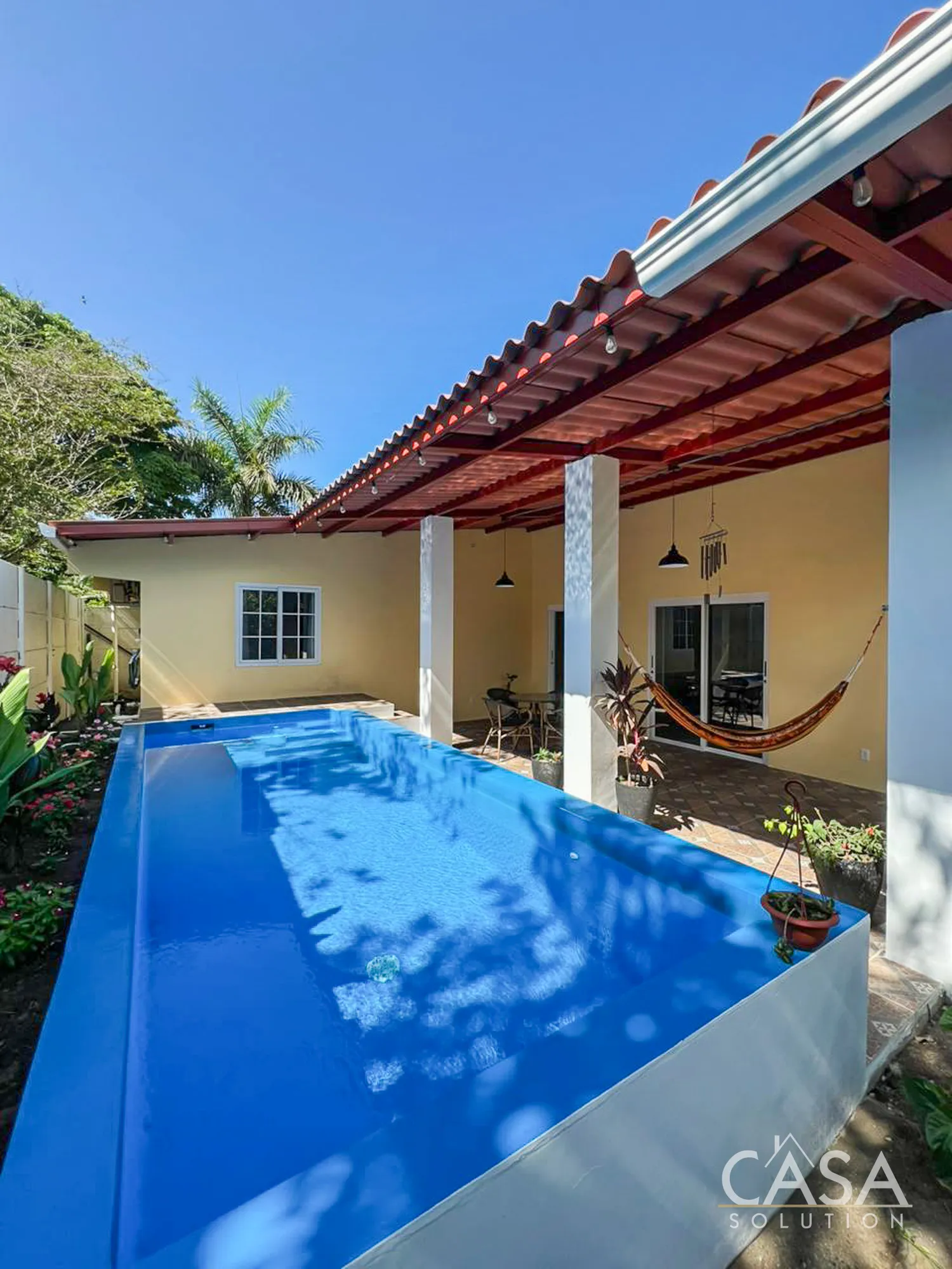 Furnished 2-bedroom home for sale in Puerto Armuelles, Chiriquí. Features include a pool, solar panels, garden with fruit trees, and gated access—just 3 minutes from the ocean